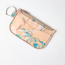Load image into Gallery viewer, Front angle view of leather key chain zipper wallet with one front pocket, zipper pocket and a shiny nickel key ring attached. Leather is a light natural color painted with water colors: brown, turquoise and and pearlescent white dyes. Dark brown thread.